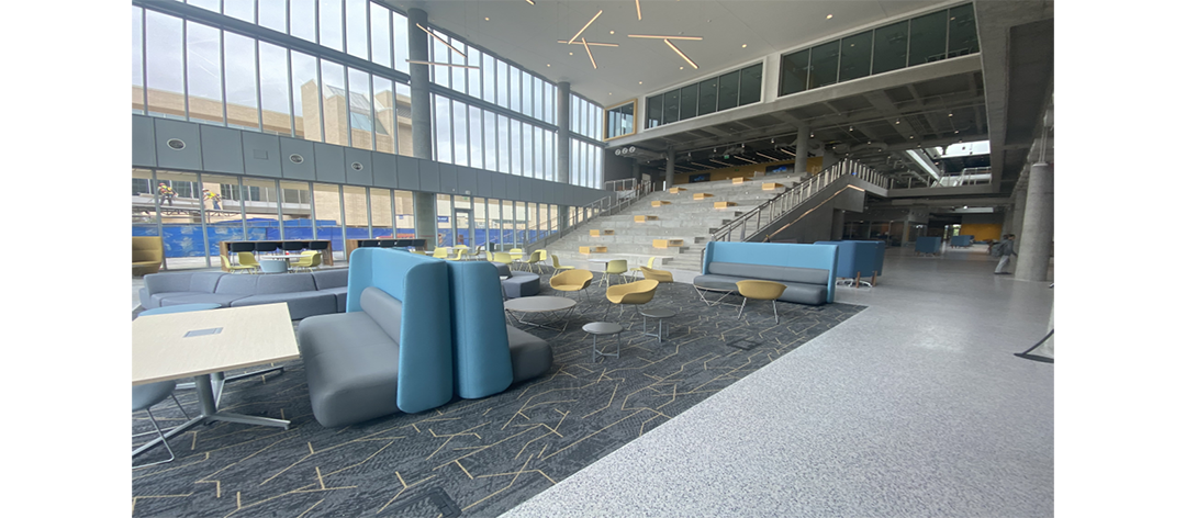 Completed open area of NW01. Foreground is seating area including tables, chairs and booths. In the backgroud you can see wide windows and a wide stair.