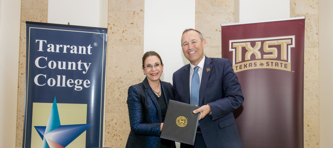 TCC Chancellor Elva LeBlanc and Texas State President Kelly Damphousse hold a folio containing the agreement documents between them and pose in front of banners for the two instituitons