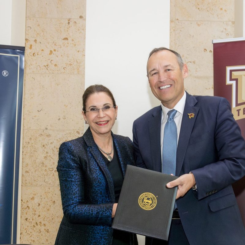 TCC Chancellor Elva LeBlanc and Texas State President Kelly Damphousse hold a folio containing the agreement documents between them and pose in front of banners for the two instituitons